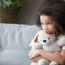 Young girl sitting on sofa hugging a teddy bear looking sad