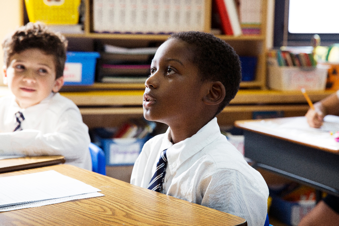 10 year old boy sitting in classroom at desk, looking up