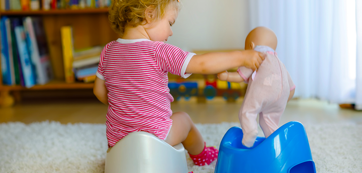 Child sitting on a potty playing with a doll on another potty.