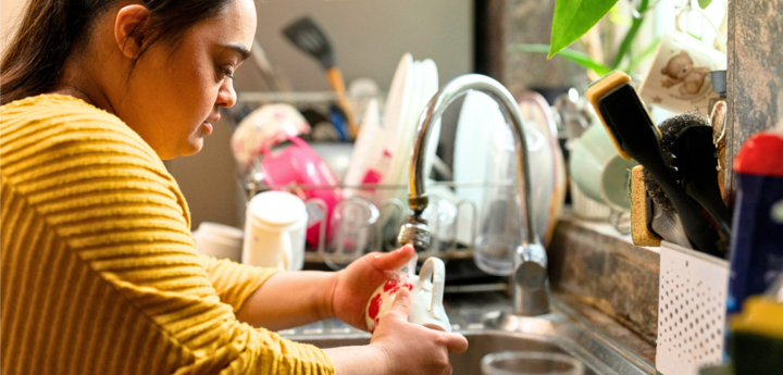 Young woman with Downs Syndrome washing a glass in the kitchen sink