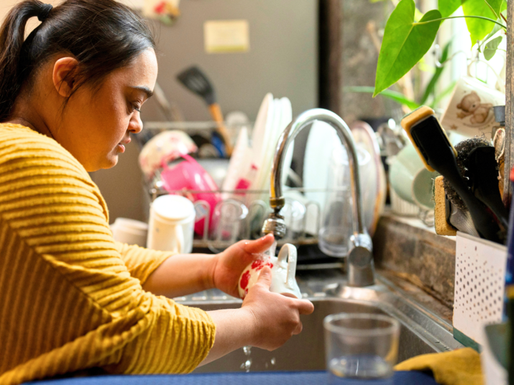 Young woman with Downs Syndrome washing a glass in the kitchen sink