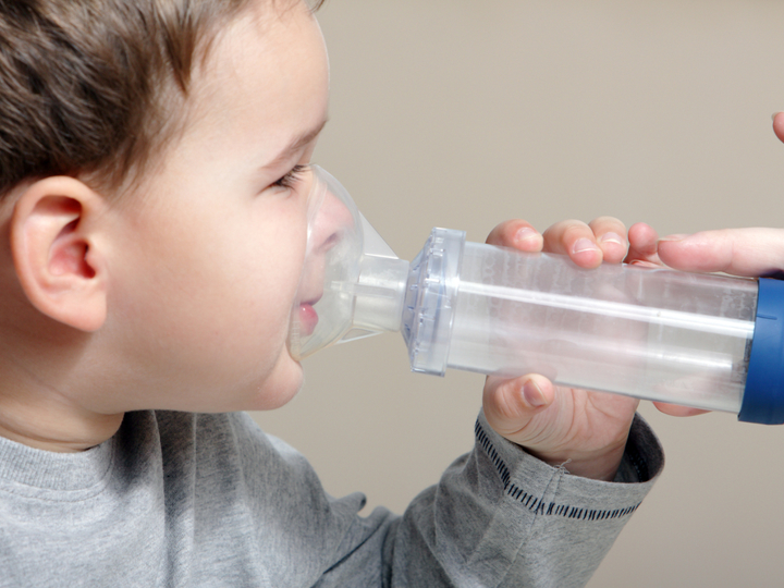 Young boy holding a spacer with an inhaler attached to his face