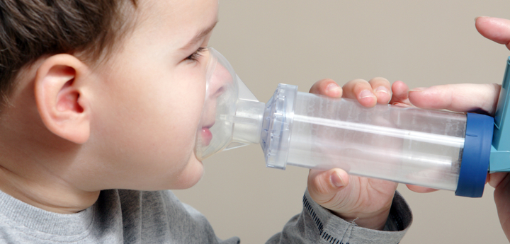 Young boy holding a spacer with an inhaler against his face