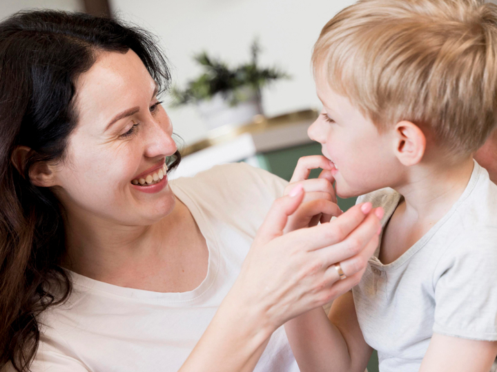 Young boy talking to his mum with his finger near his mouth. The mum is smiling and looking at him.