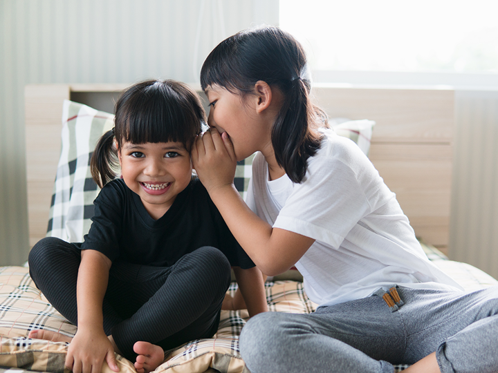 girl whispering into ear of laughing friend