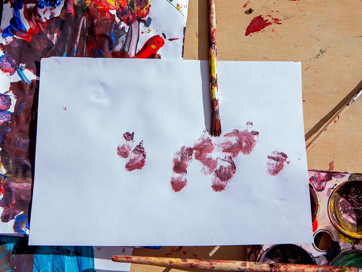 Sheet of white paper with paint on it. A paint brush covered in red paint is also lying on the sheet of paper.