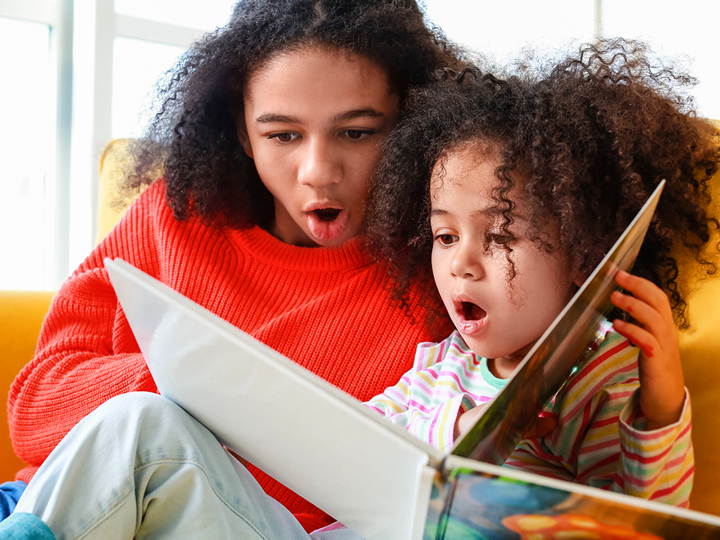 Adult and child reading book together looking shocked