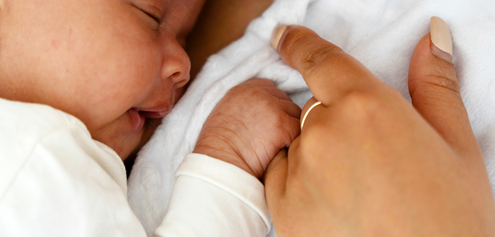 A baby gently holding an adults finger whilst resting on the adult's chest.