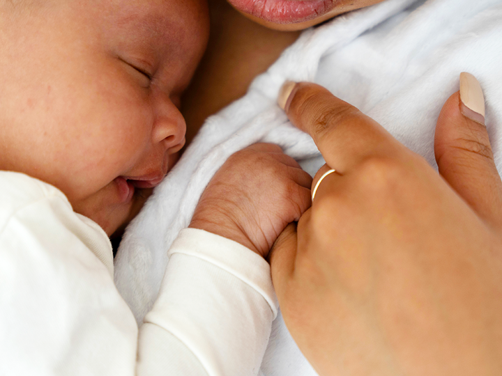 A baby gently holding an adults finger whilst resting on the adult's chest.