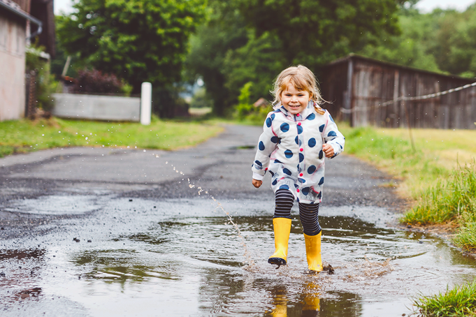 girl in wellies smiling and walking through a puddle