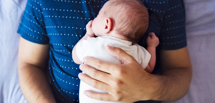 Small baby lying face down on a man's chest. The man is laying with his back on a bed.