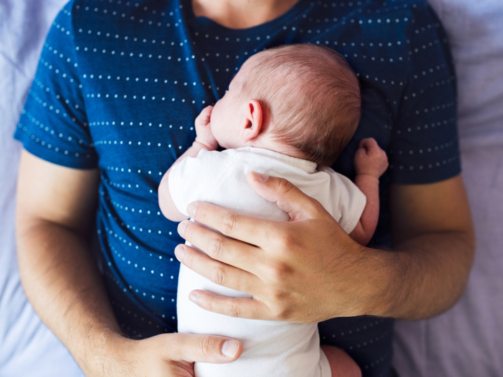 Small baby lying face down on a man's chest. The man is laying with his back on a bed.