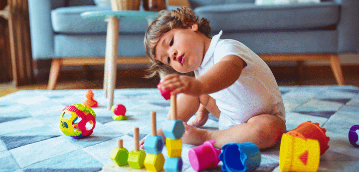 Toddler sitting on the floor in a sitting room, playing with toys on the carpet.