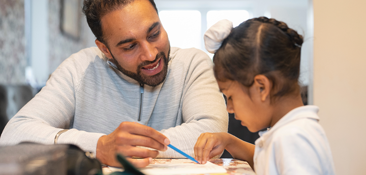 Man helping a child to learn from a book at home.