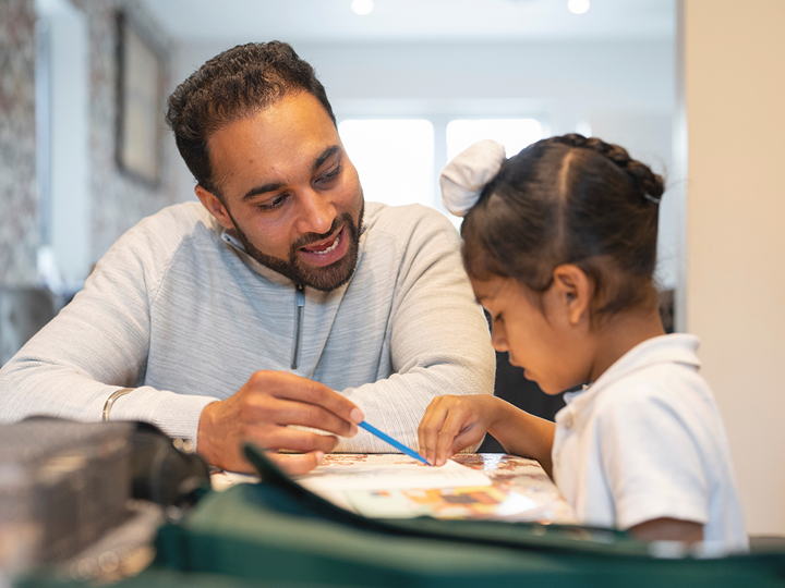 Man helping a child to learn from a book at home.