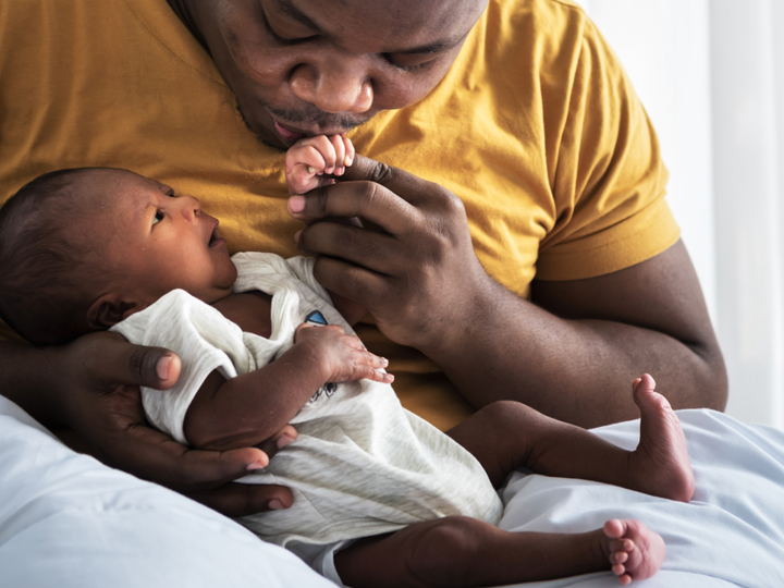 A dad holding a newborn baby in his arms and kissing their hand