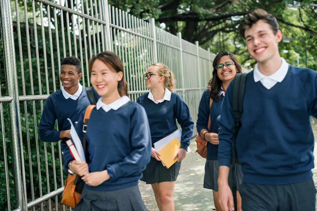 Five teenagers in school uniform smiling and laughing whilst walking down the road.