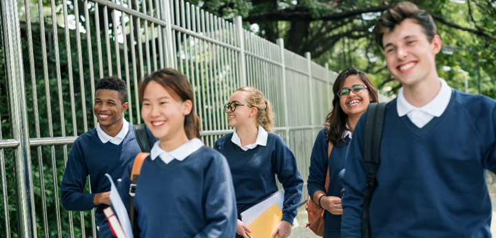 Five teenagers in school uniform smiling and laughing whilst walking down the road.