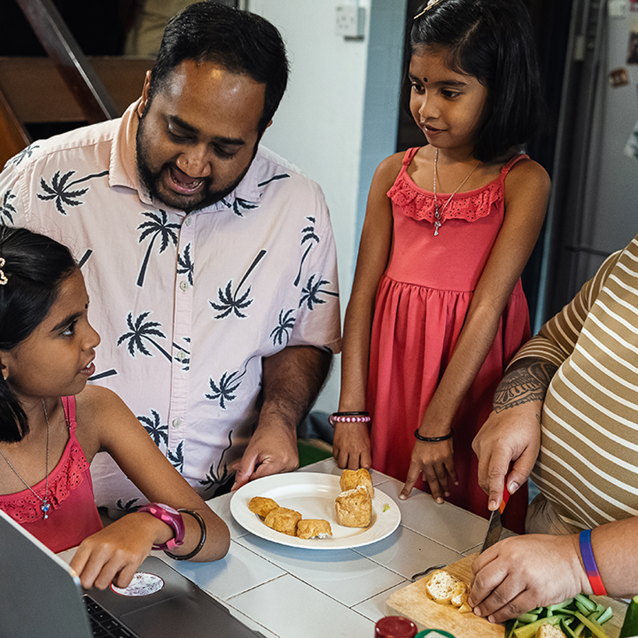 A family standing in the kitchen cooking and preparing food together.