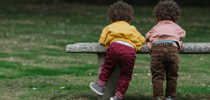 Two black toddlers playing on a bench in a park.