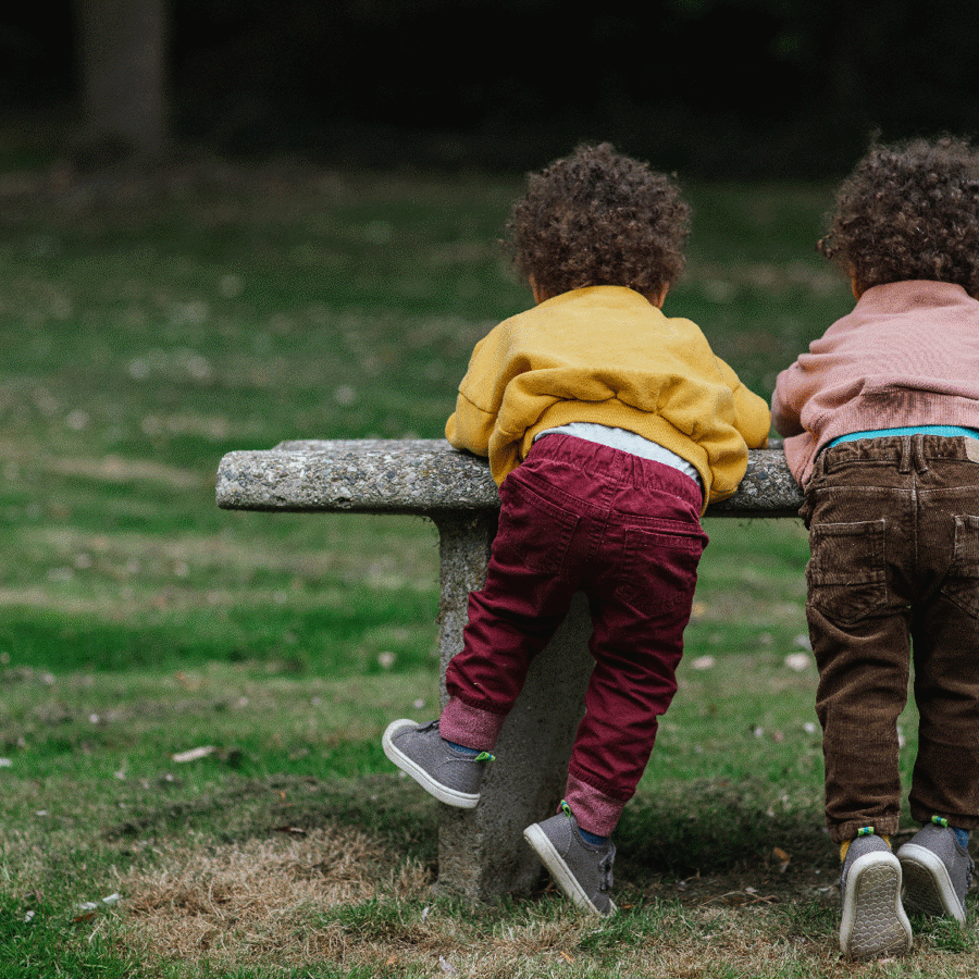 Two black toddlers playing on a bench in a park.