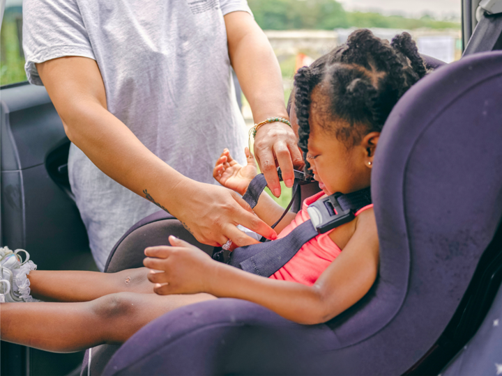 Child being clipped into a forward-facing car seat by adult