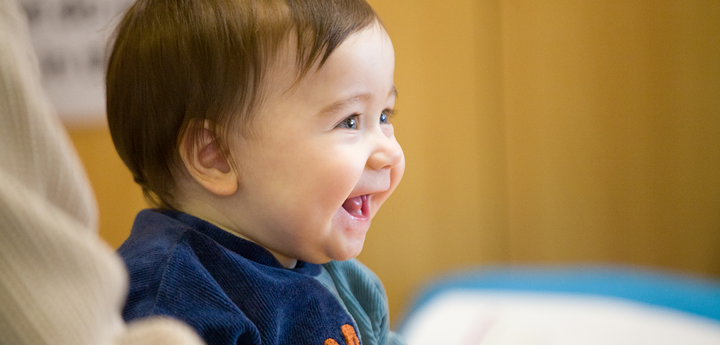 Smiling baby sitting down wearing a blue jumper.