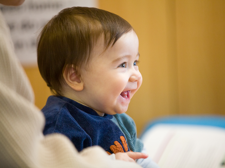 Smiling baby sitting down wearing a blue jumper.