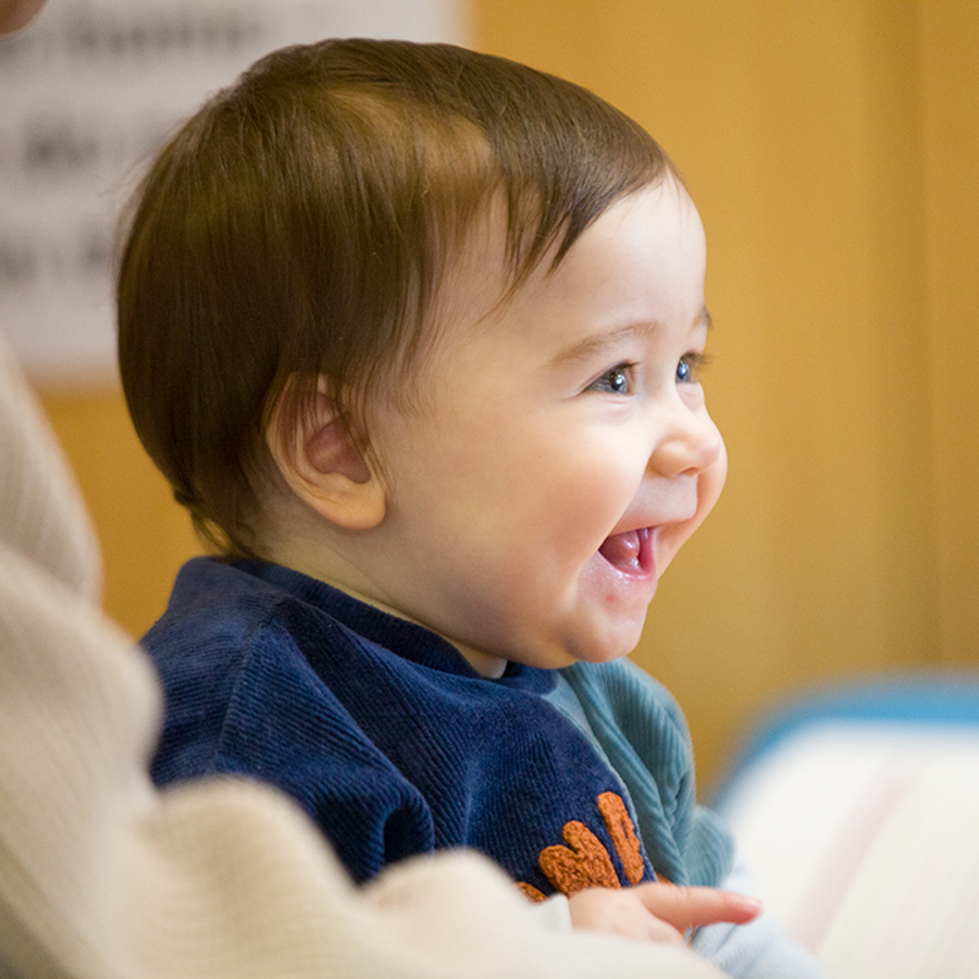 Smiling baby sitting down wearing a blue jumper.