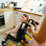 Young girl in a wheelchair smiling up at an adult standing behind her and pushing her wheelchair. They are in a kitchen.