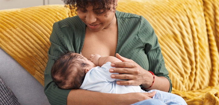 Mum sitting on sofa holding her baby whilst breastfeeding.