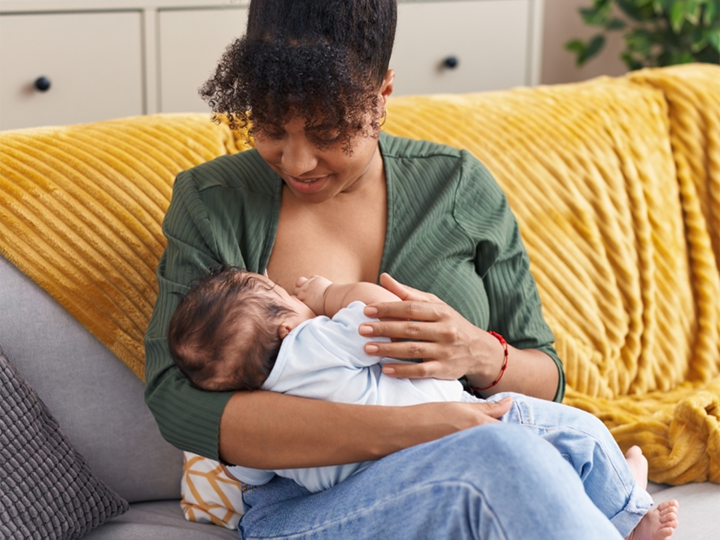 Mum sitting on sofa holding her baby whilst breastfeeding.