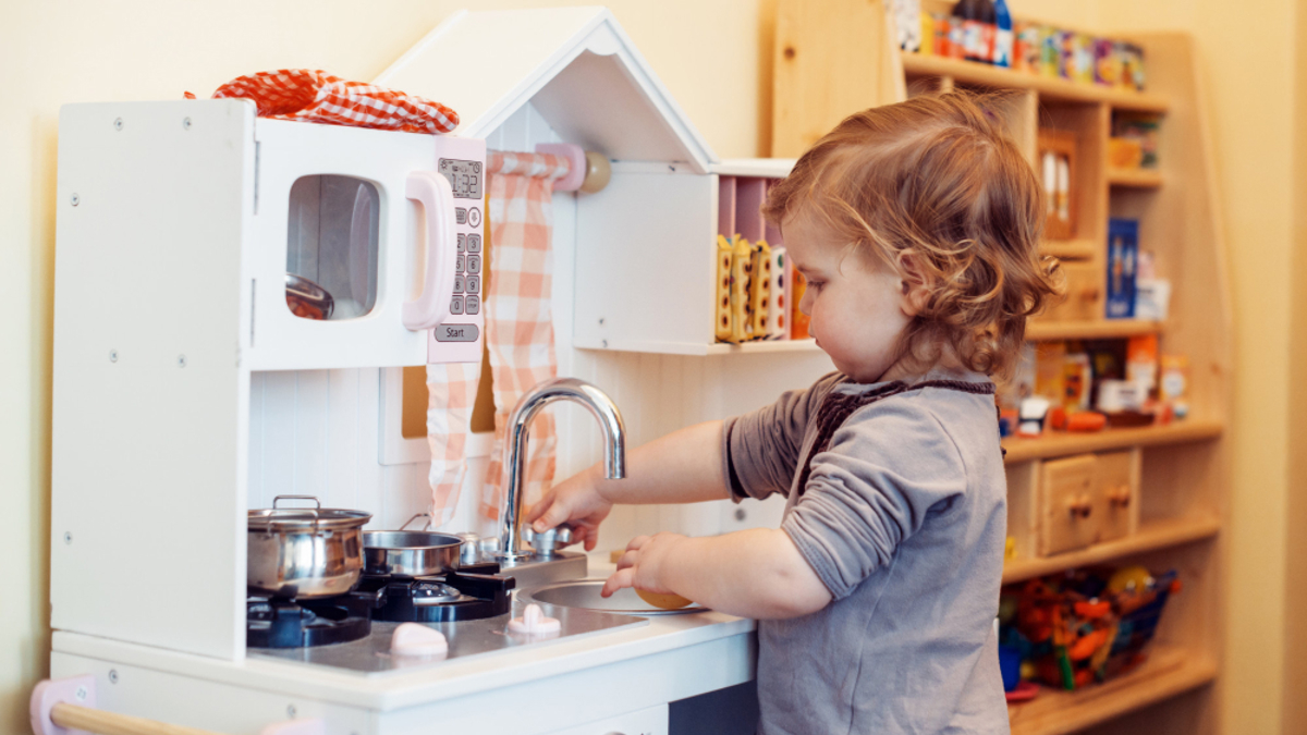 Toddler playing in a toy kitchen, turning the tap.