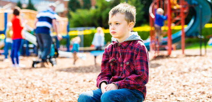 Young boy sitting alone on a low wall at a park