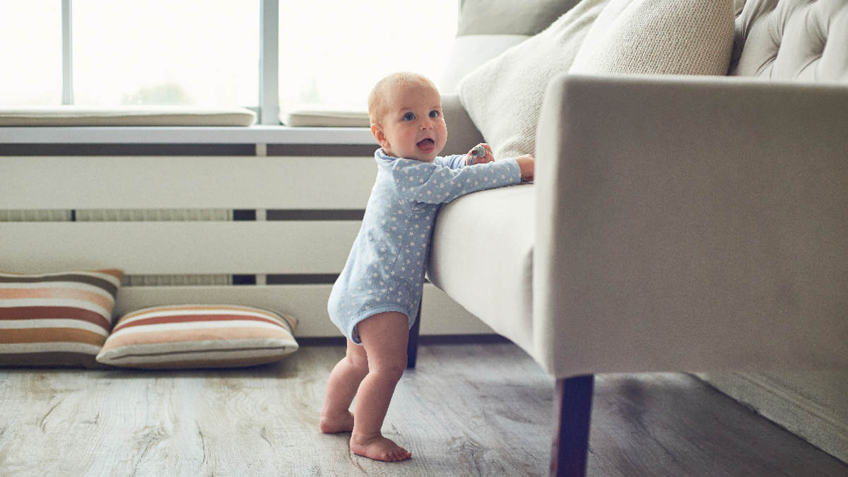 Toddler standing using a sofa to help support them as they stand.