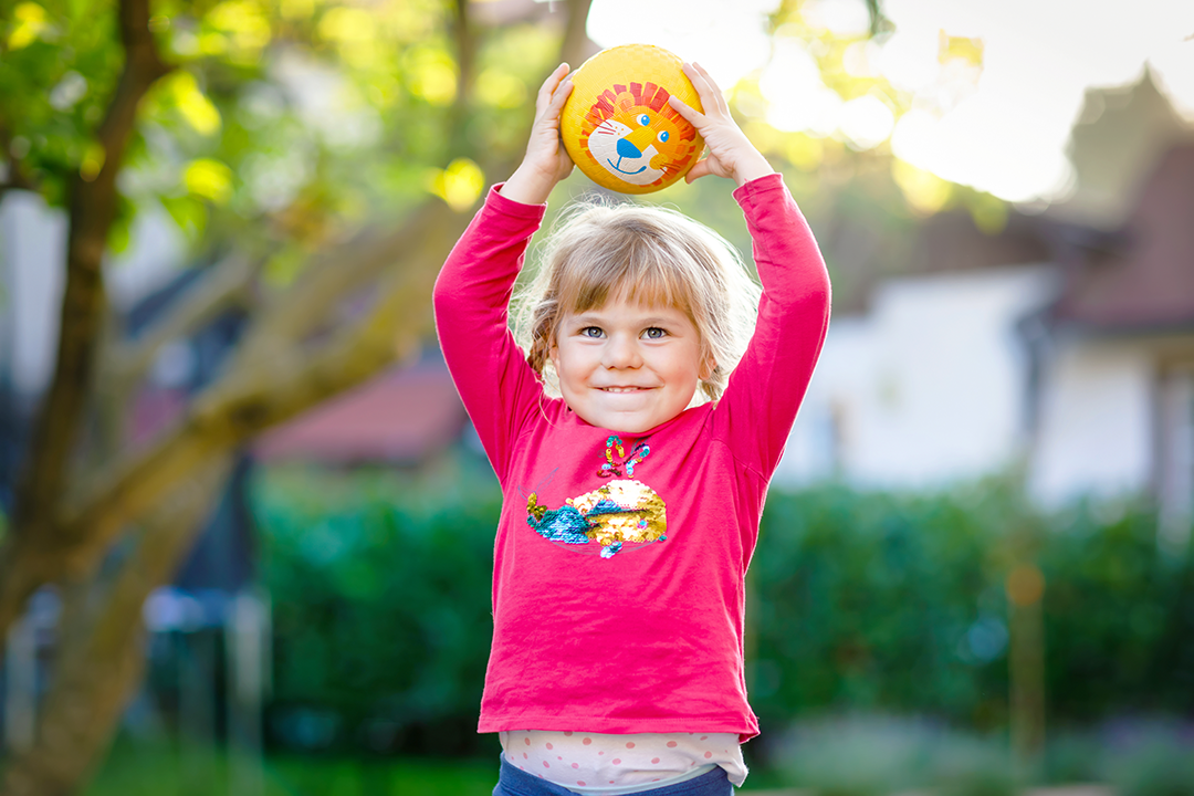 young girl holding a football over her head, ready to throw the ball.