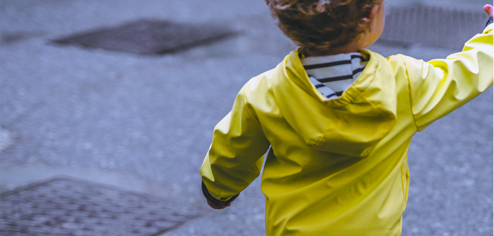 Boy toddler standing near the road in a fluorescent yellow jacket reaching his hand out.