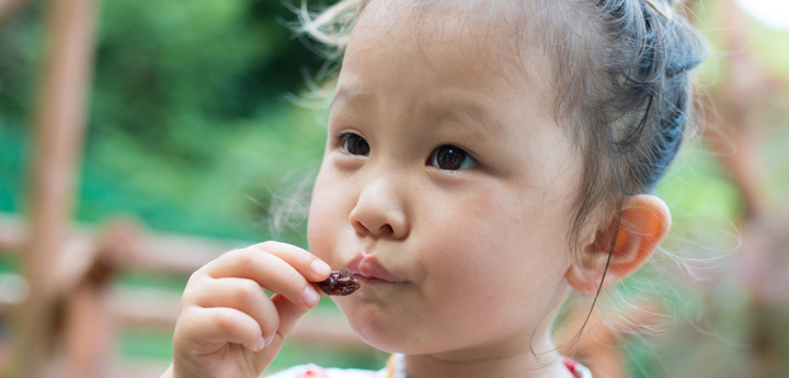 Young girl standing outside eating a raisin.