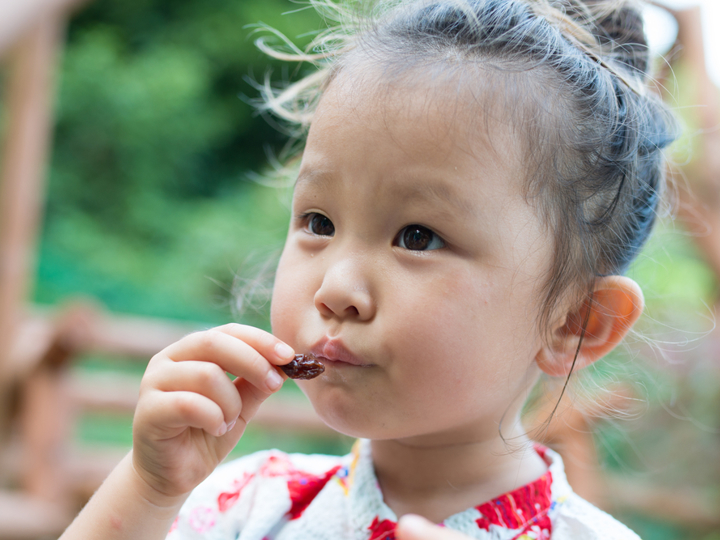 Young girl standing outside eating a raisin.