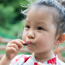 Young girl standing outside eating a raisin.