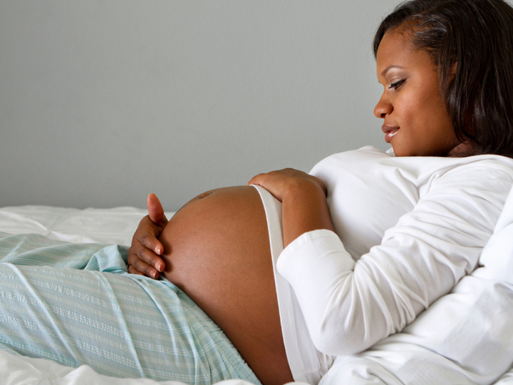 Pregnant woman lying on bed holding her stomach