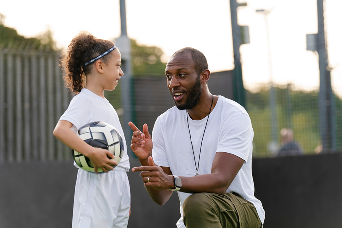 man kneeling down instructing child holding football