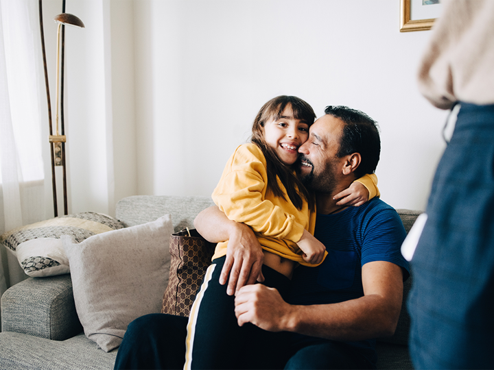 Child sitting on the lap of adult on a sofa. Both child and adult are laughing.