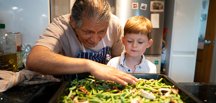 Elderly man and boy looking at green beans on baking tray.