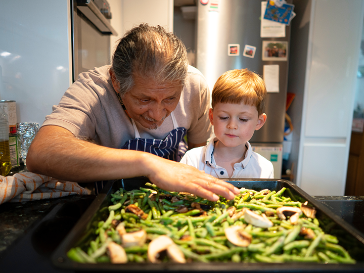 Elderly man and boy looking at green beans on baking tray.