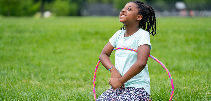 Young girl sitting in the middle of a grass field with a hula hoop around her.