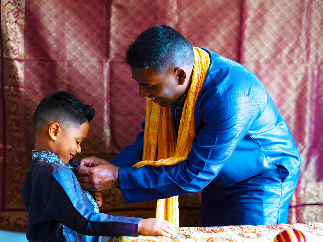 Young boy being dressed by adult in traditional dress.