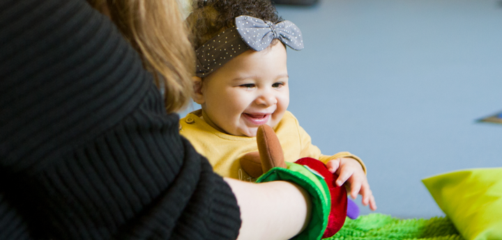 A child giggling with a lady sitting in front of the child with a hand puppet on.