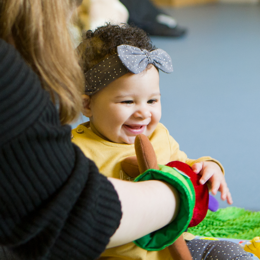 A child giggling with a lady sitting in front of the child with a hand puppet on.