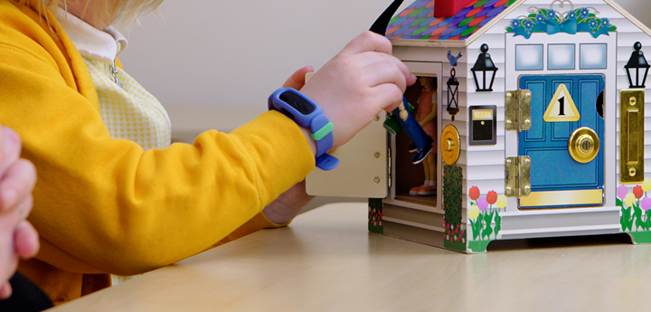 Child in yellow cardigan playing with a toy house